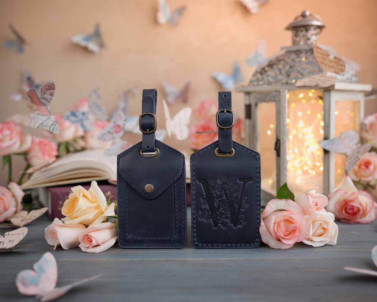 Blueberry navy leather luggage tag showing the floral initial front and address-card back, staged with roses