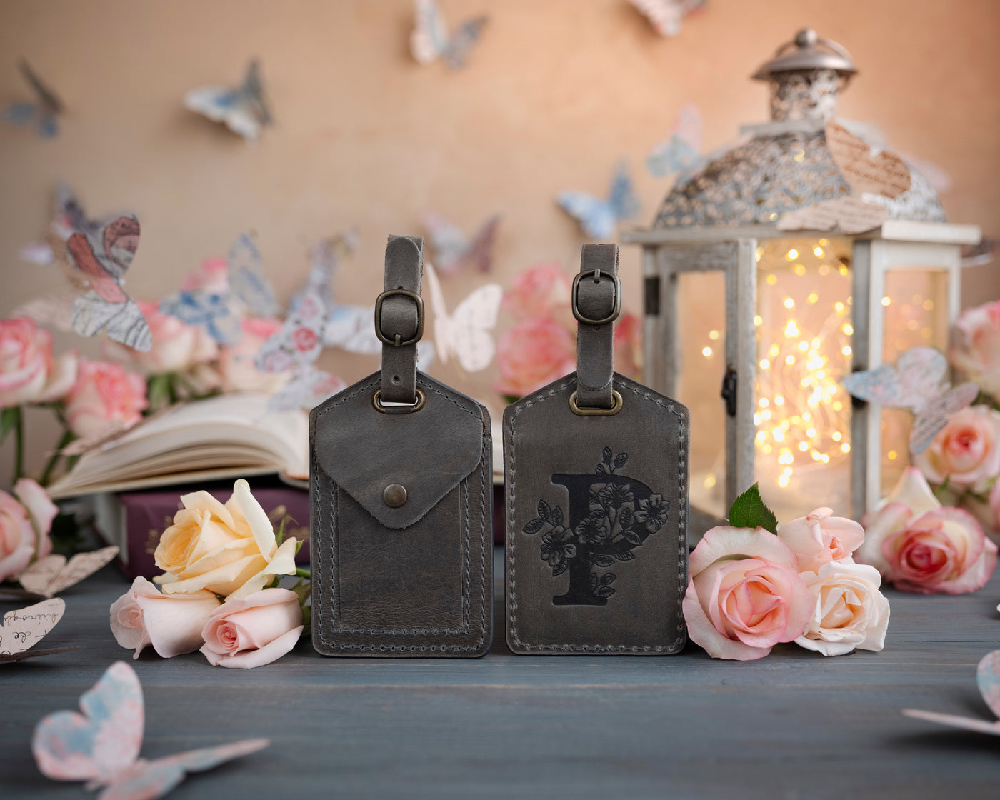 Country gray leather luggage tag showing the floral initial front and address-card back, staged with roses
