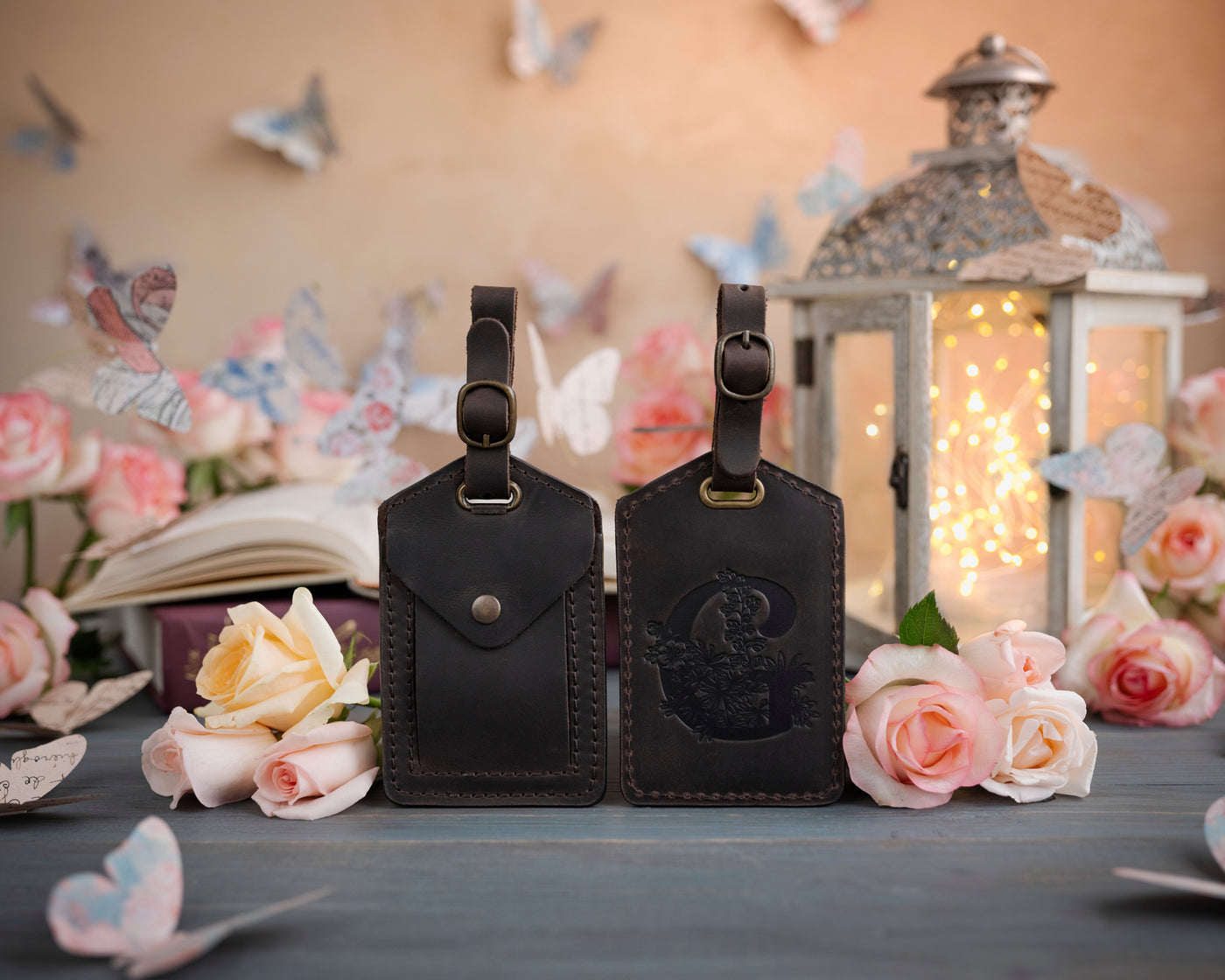 Dark espresso leather luggage tag showing the floral initial front and address-card back, staged with roses
