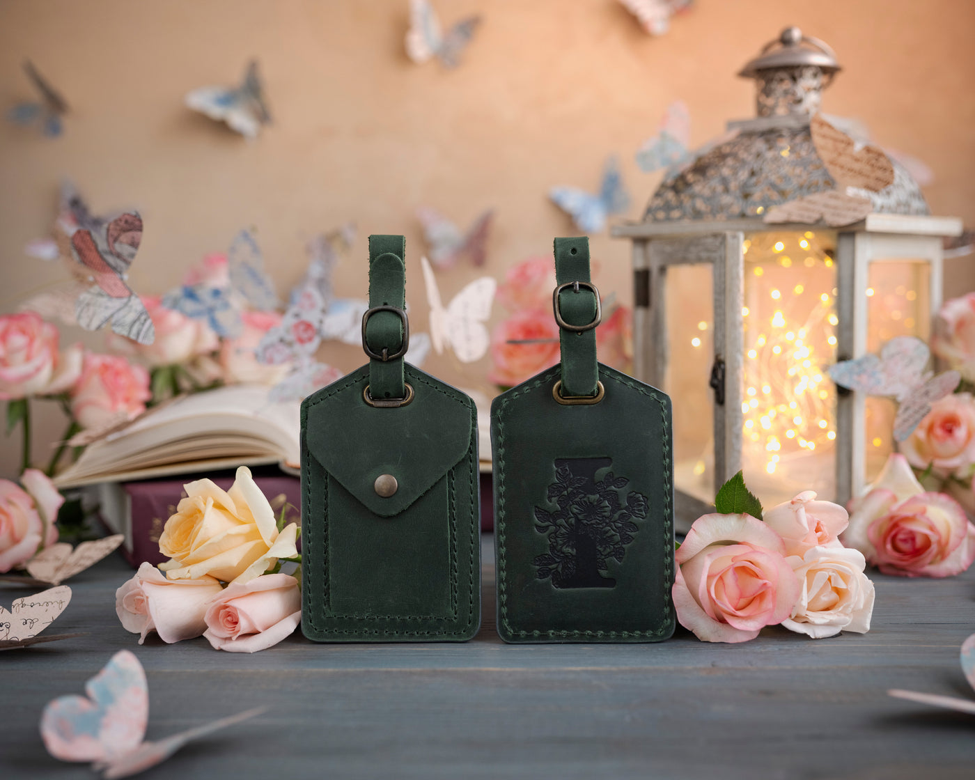 Forest green leather luggage tag showing the floral initial front and address-card back, staged with roses