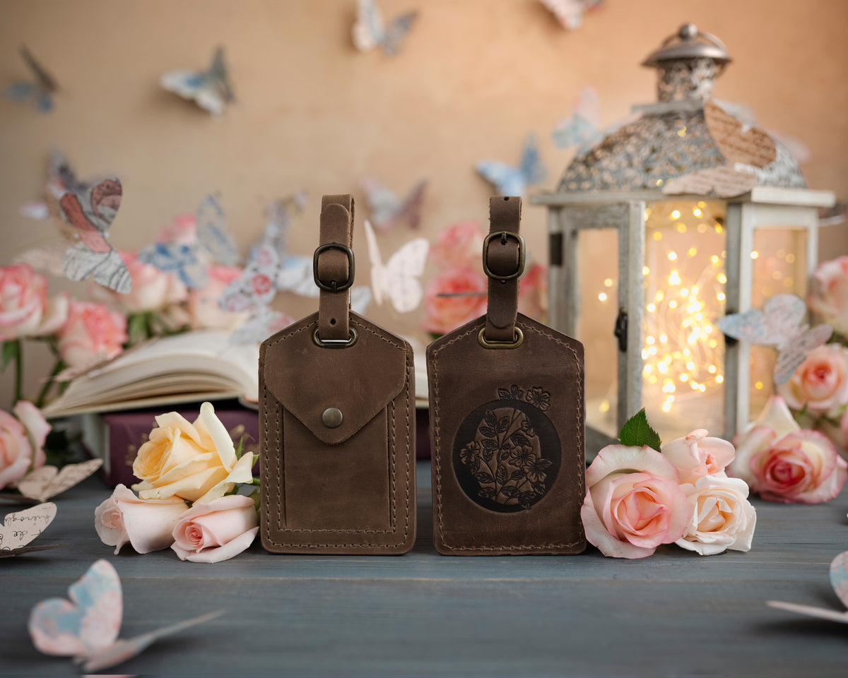 Sicilian brown leather luggage tag showing the floral initial front and address-card back, staged with roses