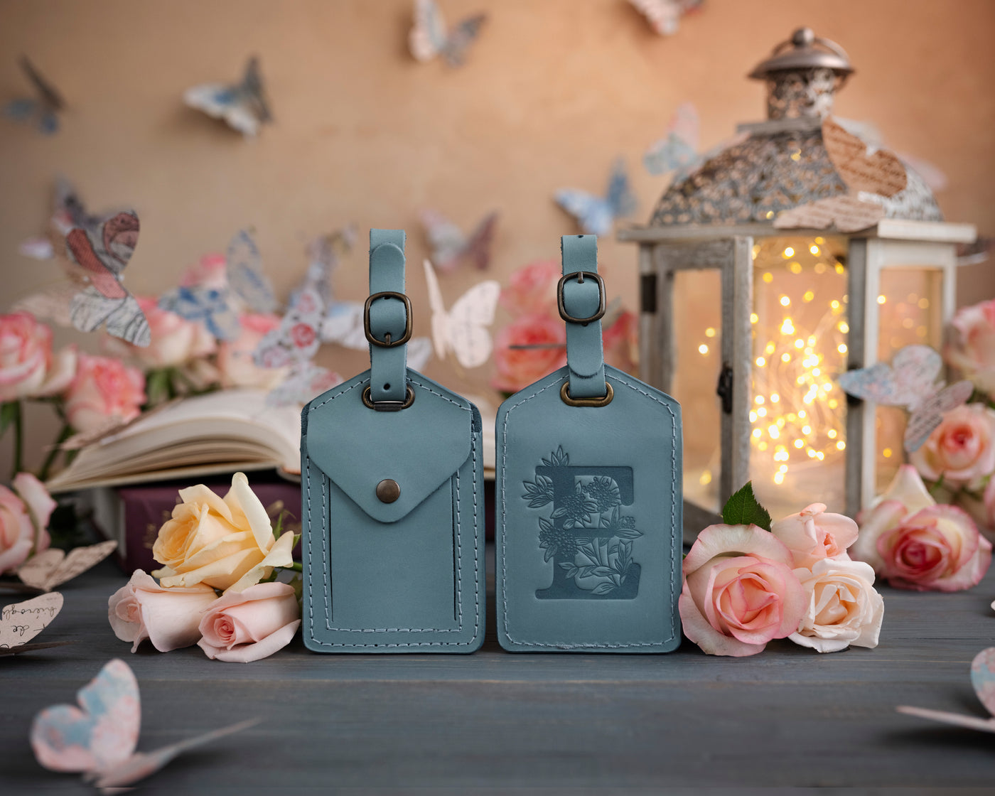 Turquoise leather luggage tag showing the floral initial front and address-card back, staged with roses