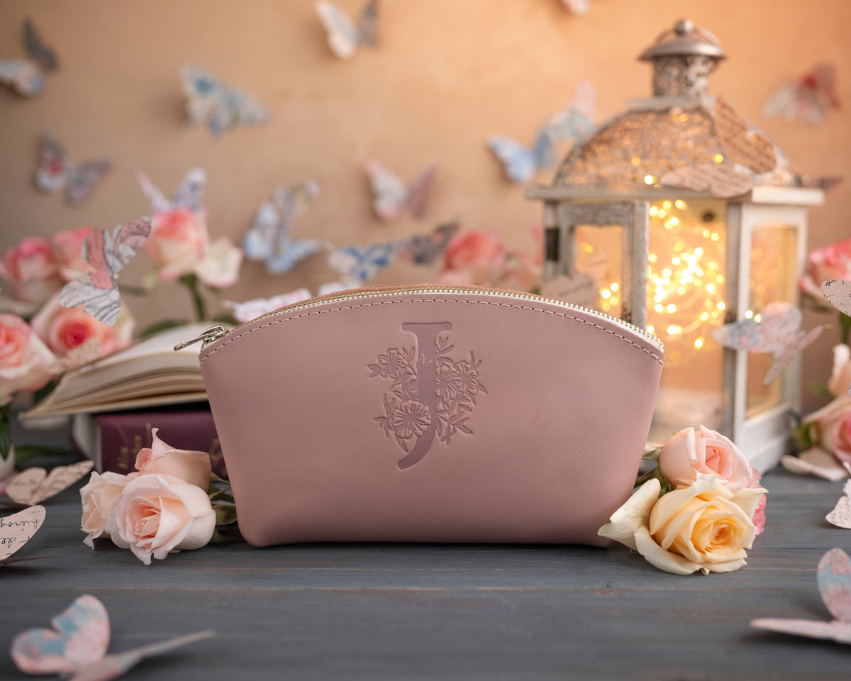 Blush pink leather makeup bag with a delicate floral monogram deboss among scattered roses