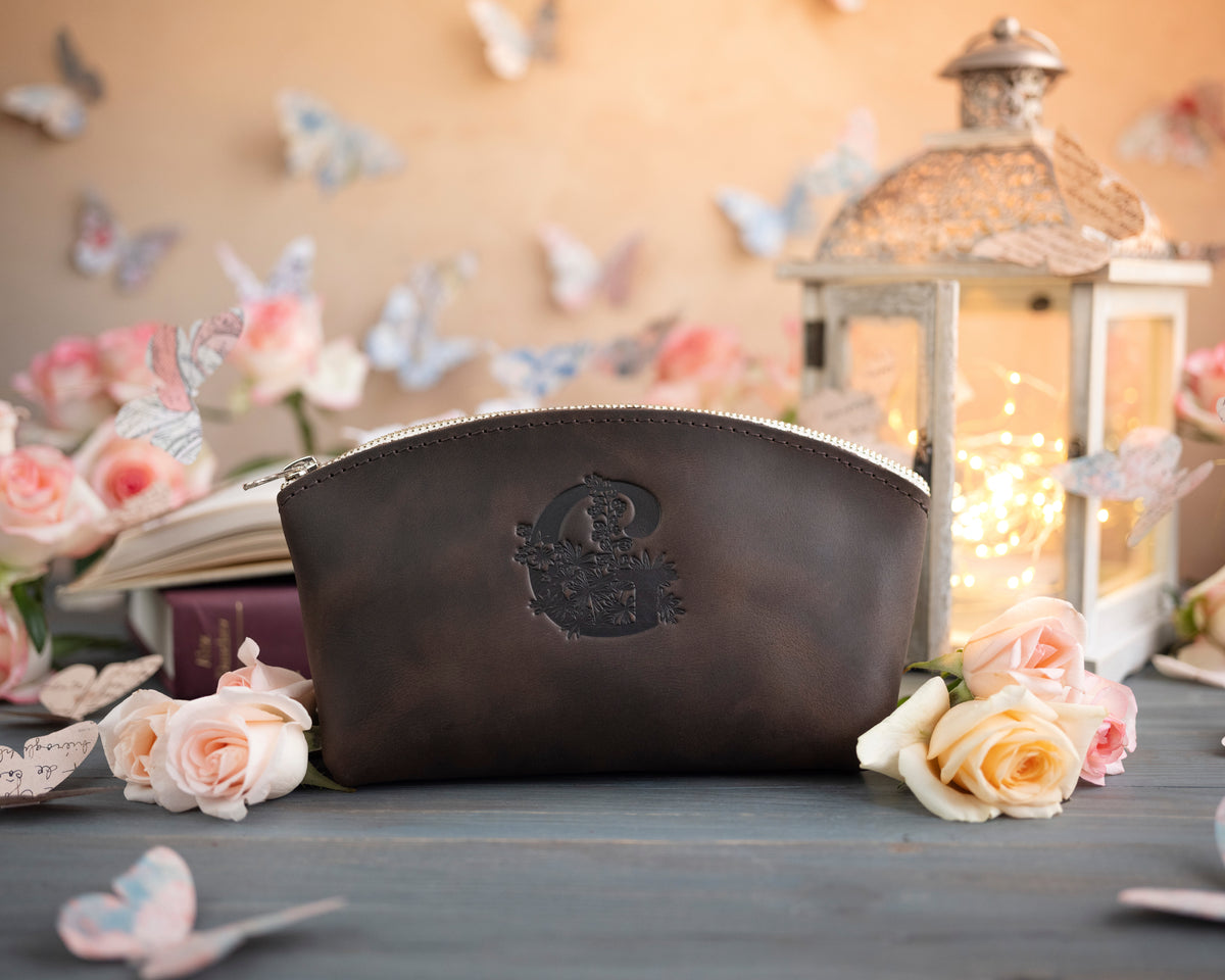 Dark espresso leather makeup pouch with an ornate crest-style monogram deboss