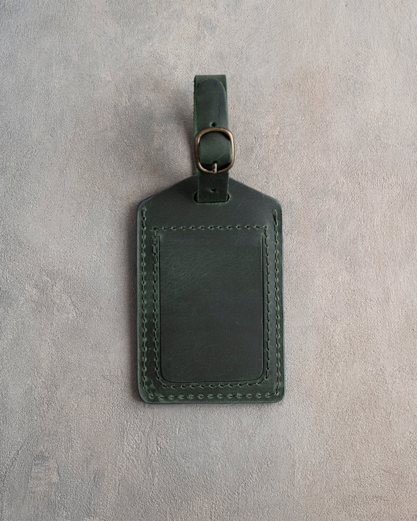 Forest green leather luggage tag back with an address-card slot, on a gray concrete surface