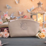 Cream leather makeup pouch with a soft floral monogram, beside a glowing lantern