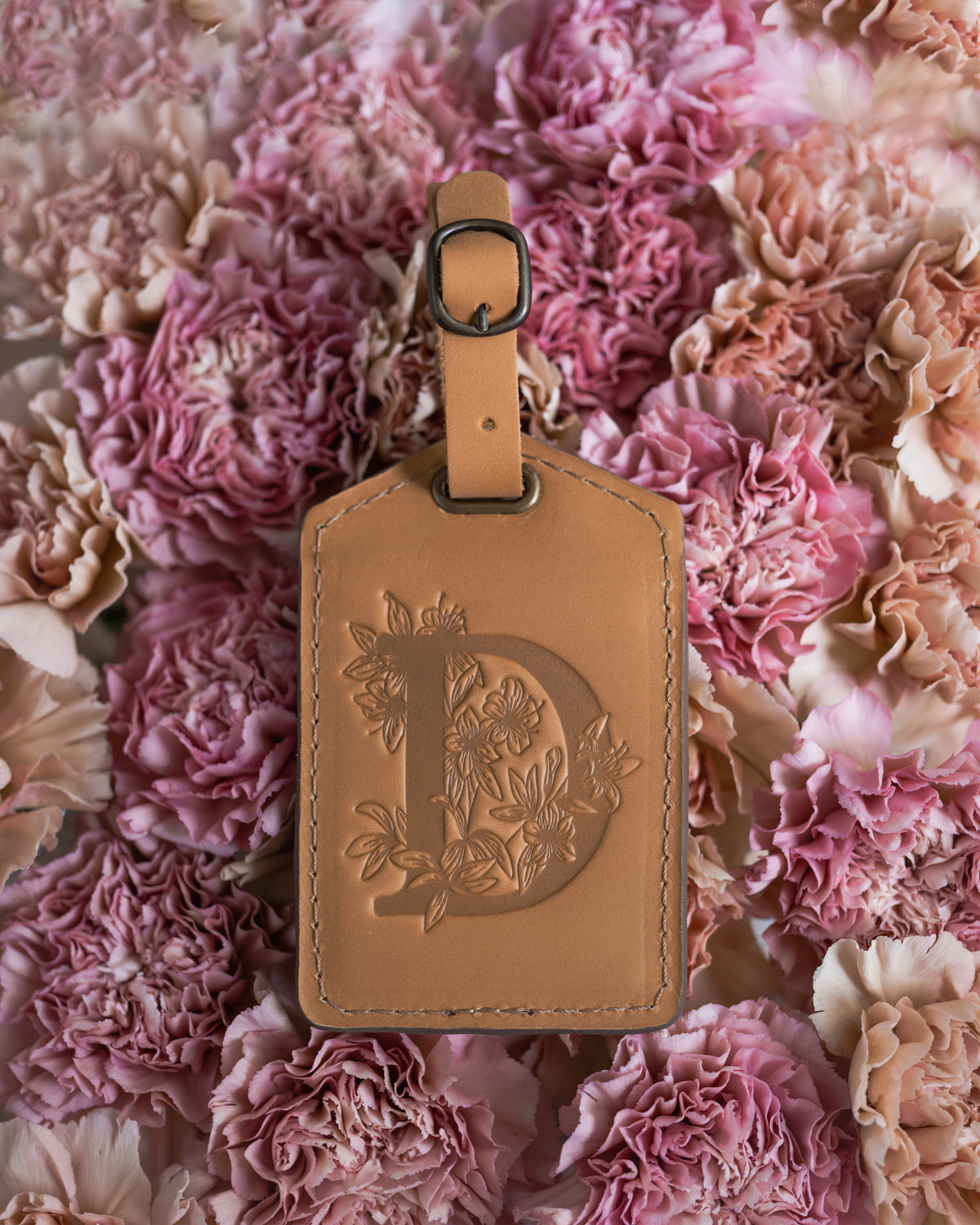 Natural caramel leather luggage tag with a floral letter D, on a bed of pink blooms