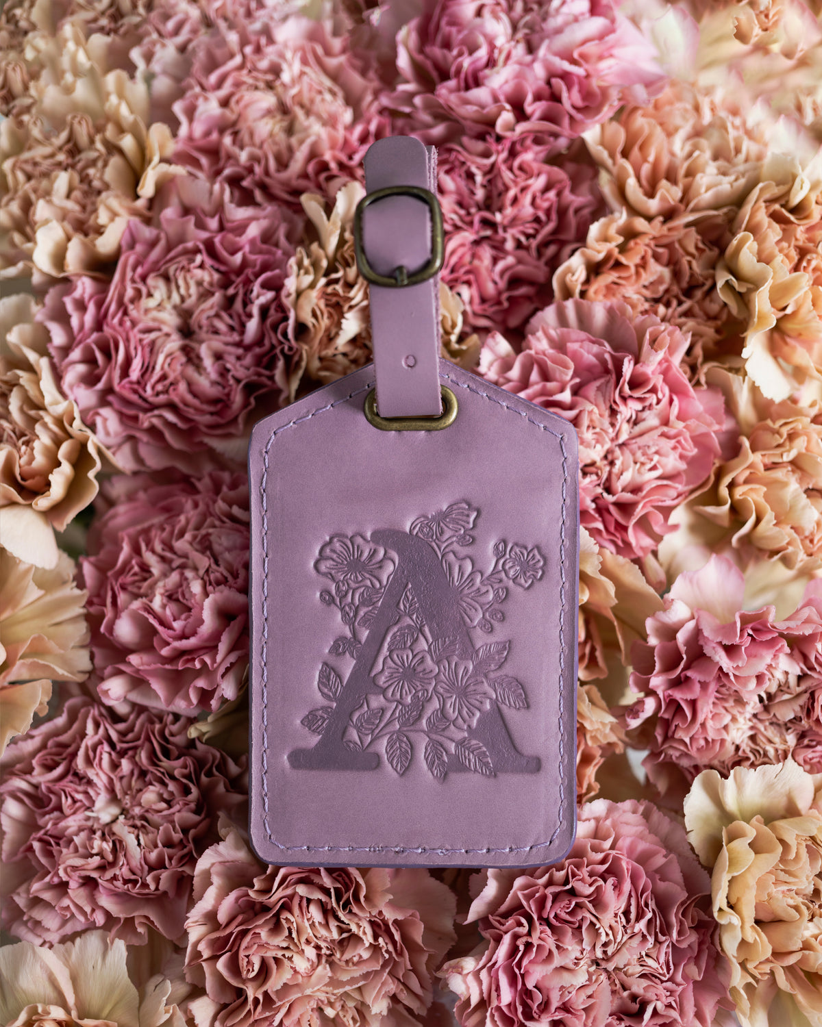 Lilac leather luggage tag with a floral letter A deboss, surrounded by pink carnations
