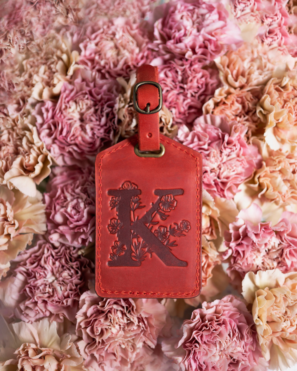 Poppy red leather luggage tag debossed with a floral letter K, on pink blooms