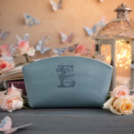 Soft blue leather makeup pouch stamped with a floral letter E, staged with roses and a lantern