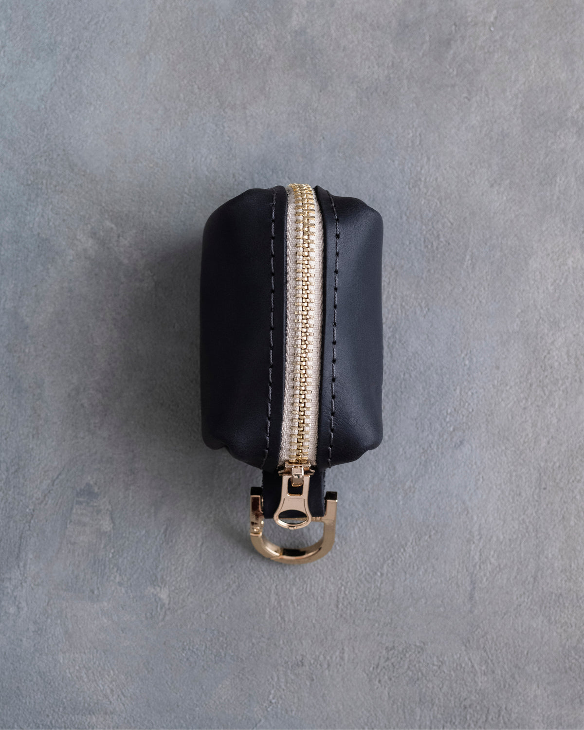 Black leather poop bag holder showing the gold zipper and clip